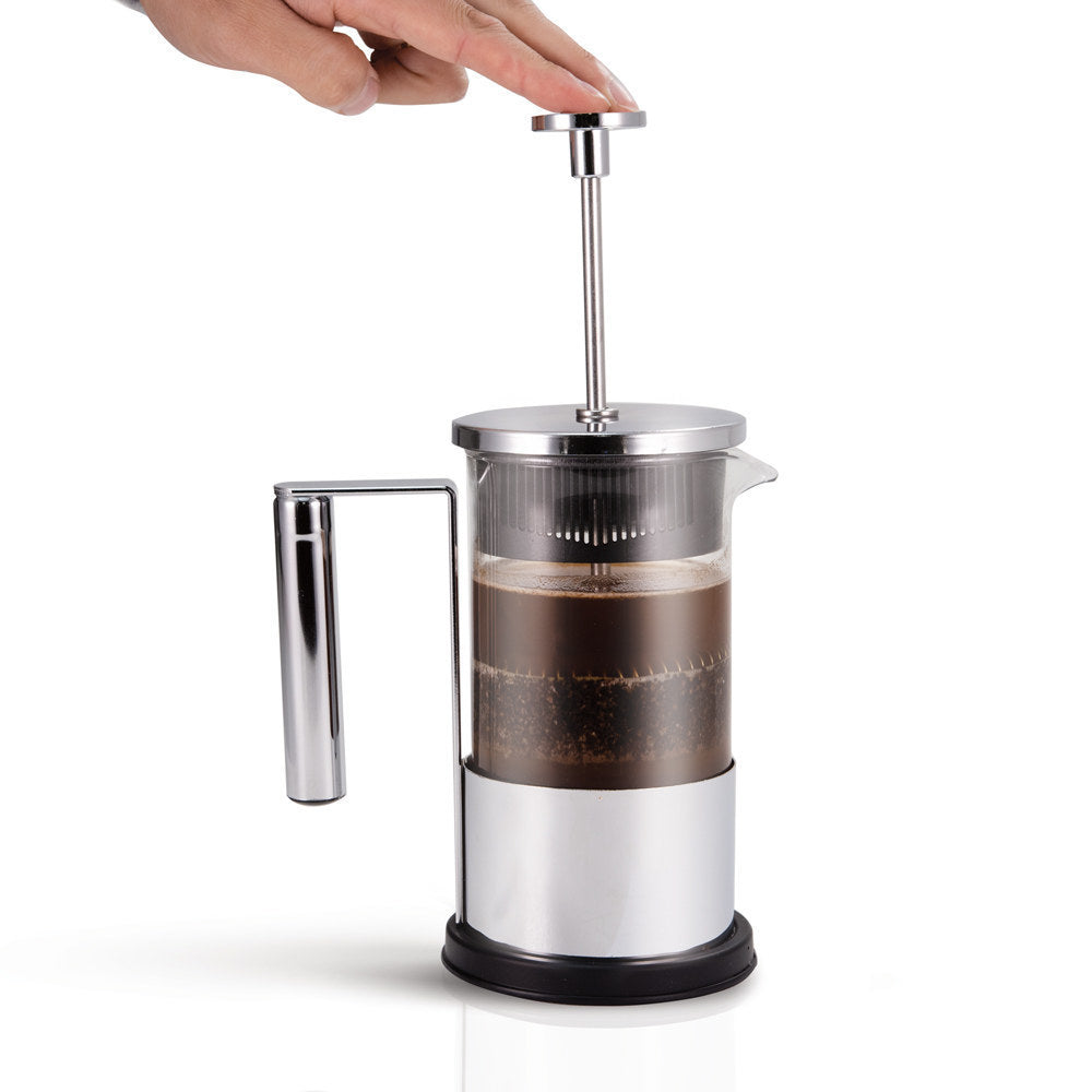 Hand pressing the plunger down on a Yama glass French press filled with brewed coffee.