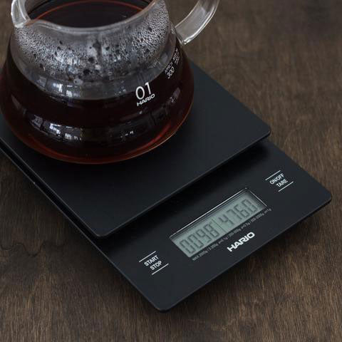 Glass coffee server resting on a Hario V60 drip scale and timer showing weight and time; server not included.