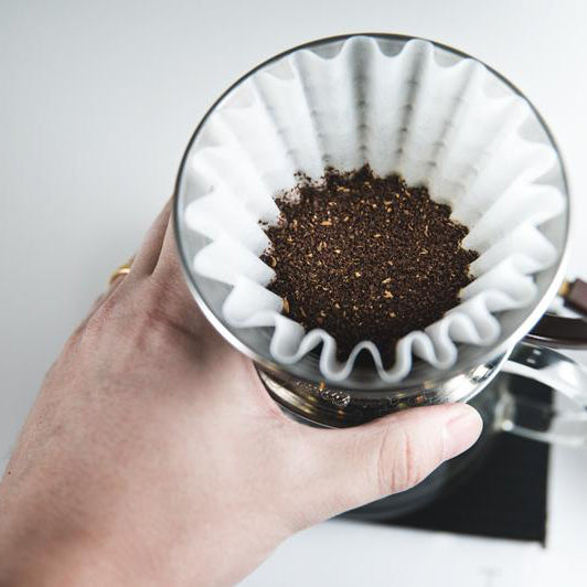 Hand holding a Kalita Wave 185 dripper filled with ground coffee in a wave paper filter; filters not included.